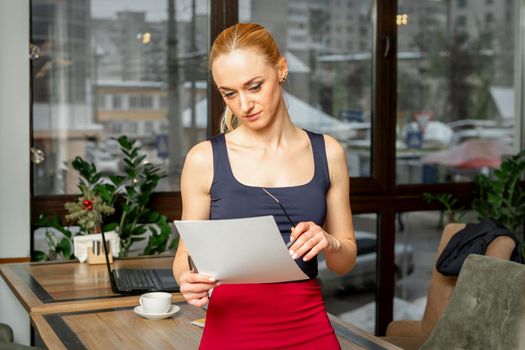 Beautiful young businesswoman looking documents while standing in the office or cafe