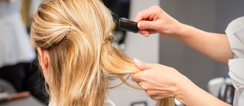 Rear View of a hairdresser combs blonde hair of the young woman in a beauty salon