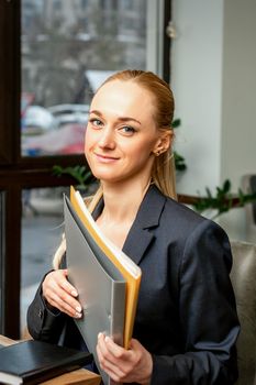 Beautiful young caucasian businesswoman holding a folder with documents sitting at the table in office or cafe