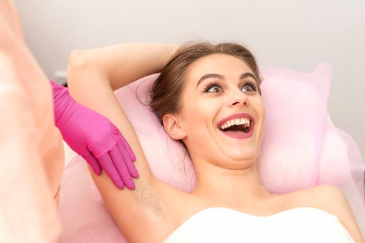Young woman during armpit examination before waxing procedure laughing in a beauty salon