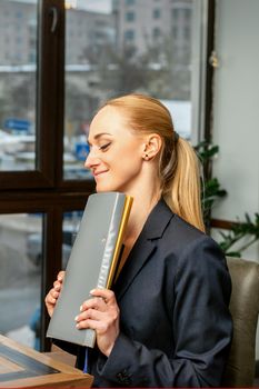 Beautiful young caucasian businesswoman holding a folder with documents sitting at the table in office or cafe