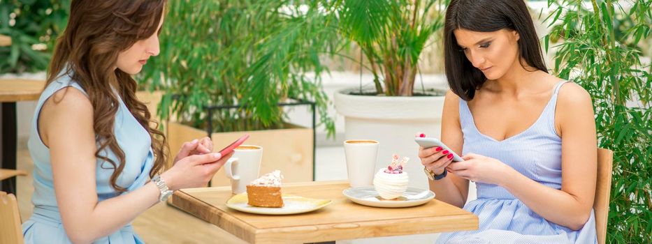 Two young women looking their smartphones while sitting in a cafe. Technology people addictions