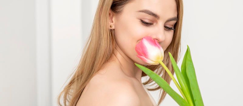 Beautiful caucasian young woman with one tulip looking on a flower against a white background