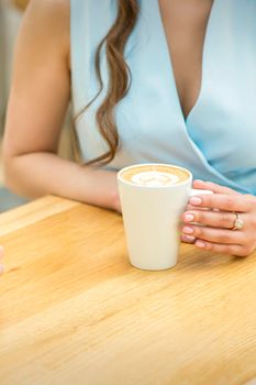 Female hands with cup of coffee on the background of a wooden table in a cafe