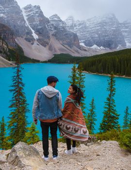 Lake moraine during a cold snowy day in Canada, turquoise waters of the Moraine lake with snow. Banff National Park of Canada Canadian Rockies. Young couple men and women standing by the lake