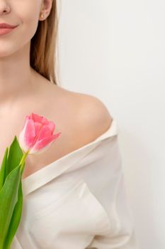 Half face of a beautiful caucasian young woman with one tulip against a white background