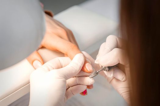 Closeup of manicure master removes nail polish uses an electric nail file in a nail salon