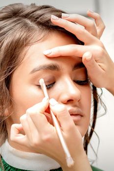Makeup artist applies eye shadow with a brush on the eye of a beautiful young caucasian woman against a white background