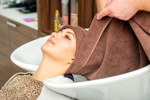 Hairdresser wraps female customer head with a towel in the sink at a hair salon