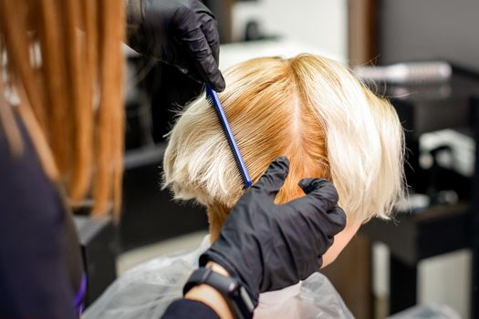 Hairdresser combing female short blonde hair before dyeing in a hair salon