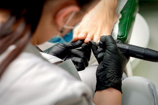 Pedicure master removes corns and cuticles with electric file machine on female toes in a nail salon