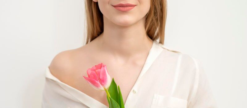 Half face of a beautiful caucasian young woman with one tulip against a white background