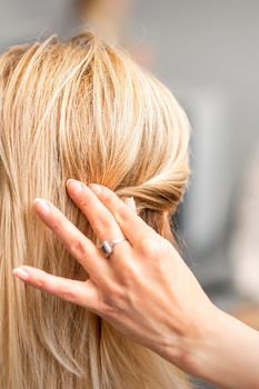Back view of the female hand of hairdresser models a hairstyle of a young blonde woman in a hair salon