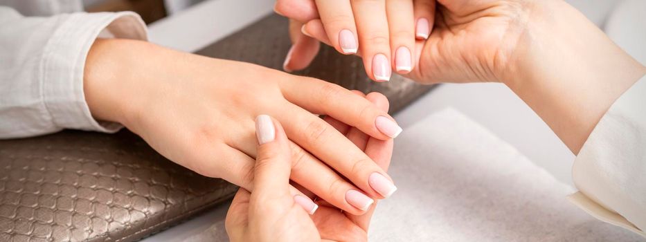 Manicure master holds hands of a young woman showing finished manicure on fingers in a nail salon