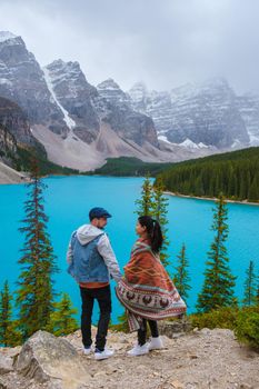 Lake moraine during a cold snowy day in Canada, turquoise waters of the Moraine lake with snow. Banff National Park of Canada Canadian Rockies. Young couple men and women standing by the lake