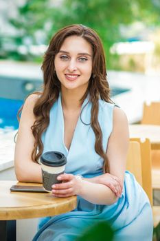 A beautiful young caucasian woman sitting at the table with a cup of hot drink near the pool