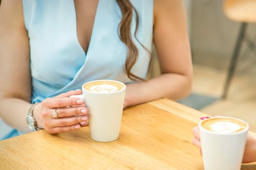 Female hands with cups of coffee on the background of a wooden table in a cafe