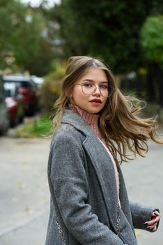 young beautiful girl posing on the street. Dressed in a stylish gray coat and knitted pink sweater.