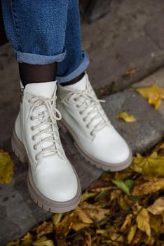 Female legs in a jeans and white fashion boots with laces. fallen leaves on the sidewalk