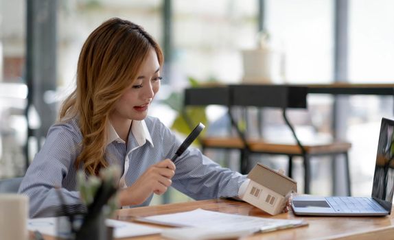 Close up of businesswomen holding magnifying glass finding a wooden shape of a house, realtor, agent, insurance, developer, planning