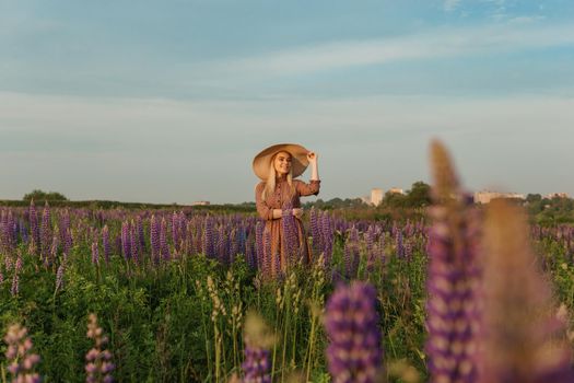 A beautiful woman in a straw hat walks in a field with purple flowers. A walk in nature in the lupin field.