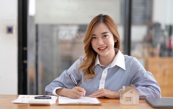 Miniature house in the hands of an Asian woman real estate agent home loan working at the office. Looking at the camera..