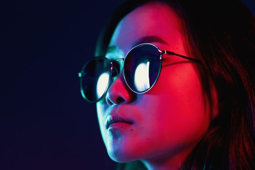 Millennial pretty asian girl with long hairstyle with neon light. Mysterious hipster teenager in glasses
