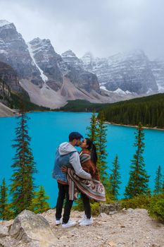 Lake moraine during a cold snowy day in Canada, turquoise waters of the Moraine lake with snow. Banff National Park of Canada Canadian Rockies. Young couple men and women standing by the lake