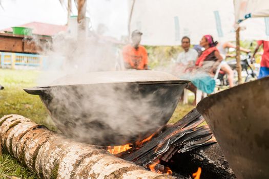 Unrecognizable indigenous people preparing a broth over a pot on a campfire
