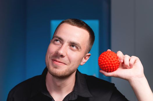 The hand of a man holds a rubber ball, a portrait of a young caucasian masseur doctor, smiles and thinks about something.