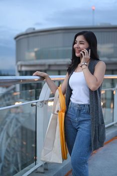 Attractive asian woman with shopping bags standing on terrace of modern building overlooking the city. Lifestyle concept.