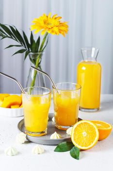 Glasses with orange juice, orange slices and mango on a gray background.