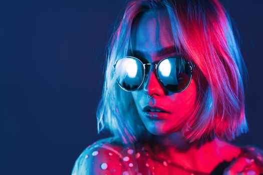 Close up portrait of millennial pretty girl with short hairstyle with neon light. Dyed blue and pink hair. Mysterious hipster teenager in glasses