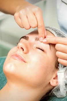 Beautician's hands make massage on eyebrow for a woman while a facial massage in cosmetology clinic center