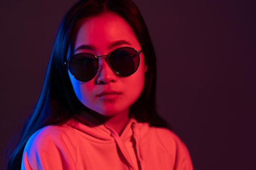 Millennial pretty asian girl with long hairstyle with neon light. Mysterious hipster teenager in glasses