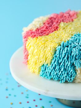 Shag cake on blue background. Funny colorful vanilla shag cake with perfect vanilla buttercream. Idea of visually striking cake decorating schemes, trendy cake. Vertical. Close up.