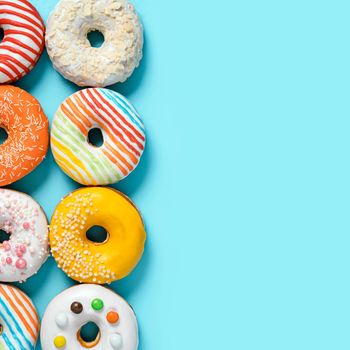 Delicious glazed donuts on blue background. Square flat lay - set of different colorful donuts or doughnuts on blue with copy space for text or design. Bright sun light with hard shadows.
