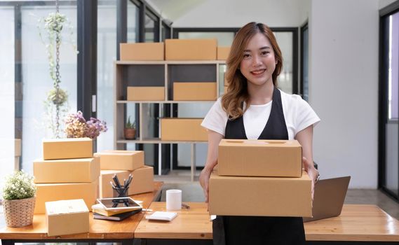 Startup SME small business entrepreneur SME or freelance Asian woman using a laptop with box, Young success Asian woman with her hand lift up, online marketing packaging box and delivery, SME concept..