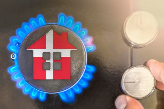 Heating season or gas use in Denmark. Concept, model of a house stands near the flame of a gas boiler on a black background. The cost of using natural gas in Denmark