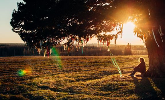 woman sitting under a lonely tree at sunset.