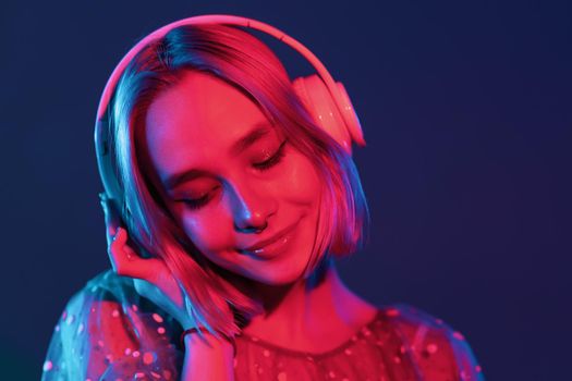 Mysterious hipster teenager listening to music with headphones. Portrait of millennial pretty girl with short hairstyle with neon light. Dyed blue and pink hair