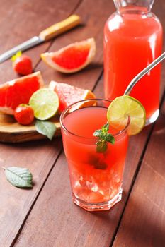 Fresh grapefruit juice in a glass with grapefruit pieces, lime and mint on a wooden background. vertical photo