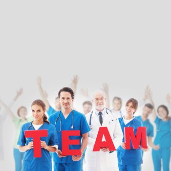 Group portrait of happy medical doctors workers holding TEAM letters on gray background, blue uniform