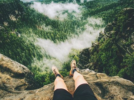 Hiker legs hiking in fall nature. Guy just relax on mountain top and enjoy view.  Feets in trekking shoes and legs short running trousers 