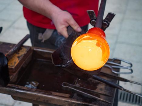 Glass blower forming beautiful piece of glass by traditional hand method. A glass crafter is burning and blowing an art piece.
