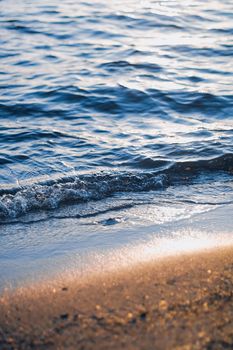 Blue sea waves and golden sand in sunshine glow at sunset, sandy beach and coastal nature concept