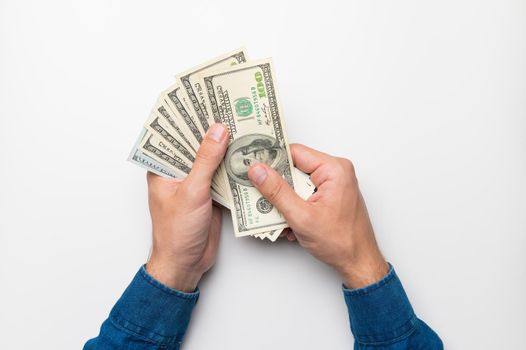 A first-person photograph showing male hands holding a fan of one hundred dollar bills against a white background. studio shot.