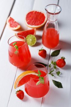 Fresh grapefruit juice in a glass with grapefruit pieces, lime and mint on a wooden background. vertical photo,selective focus