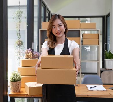 Startup SME small business entrepreneur SME or freelance Asian woman using a laptop with box, Young success Asian woman with her hand lift up, online marketing packaging box and delivery, SME concept..