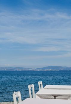 White restaurant tables on the beach in summer - travel, vacation and summer concept. The perfect lunch with a sea view